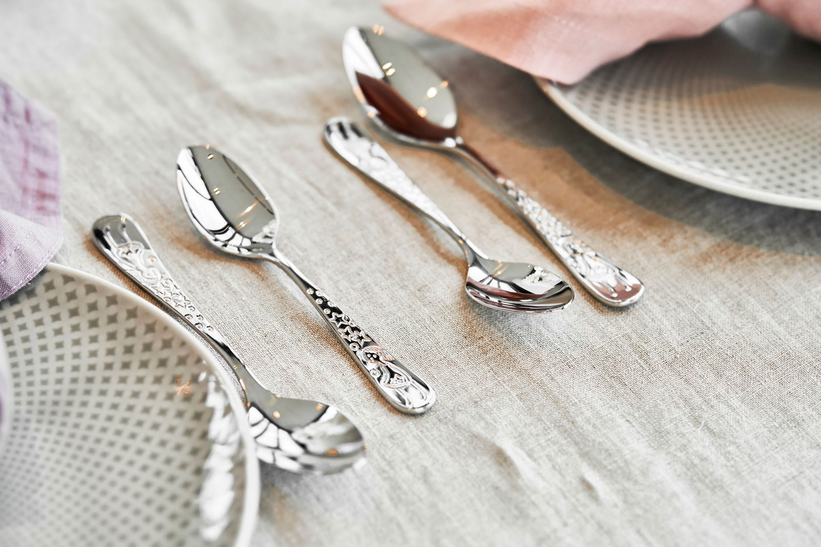 Kinderbesteck-Set mit märchenhaften Motiven, bestehend aus vier Teilen, auf einem gedeckten Tisch von schräg oben fotografiert.