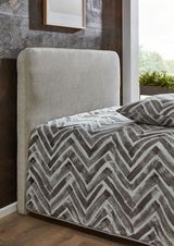 Seitliche Ansicht eines Polsterbetts mit grauem Kopfteil und gemustertem Bettbezug in einem modernen Schlafzimmer.