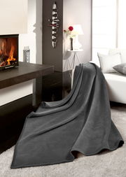 Graue Wohndecke THERMOSOFT UNI auf einem Sofa in einem modernen Wohnzimmer mit Kamin, seitliche Perspektive.