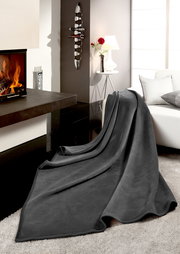 Graue Wohndecke THERMOSOFT UNI auf einem Sofa in einem modernen Wohnzimmer mit Kamin, seitliche Perspektive.