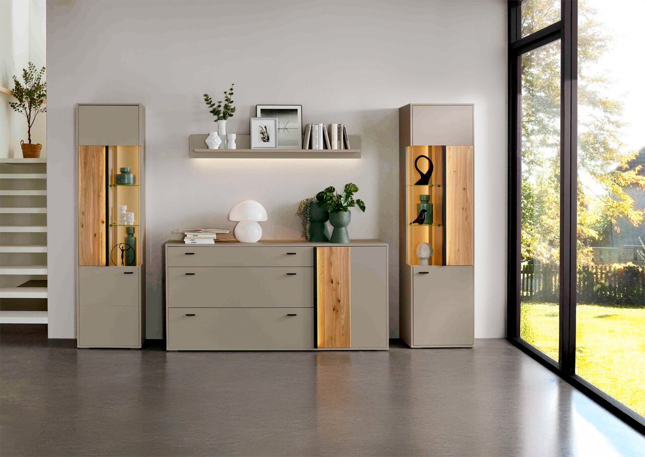 Moderne woonkamermeubels met twee vitrinekasten, een dressoir en een wandplank in een lichte, stijlvolle omgeving. De meubels zijn uitgevoerd in neutrale tinten en versierd met houten details. Het perspectief toont de meubels van voren, met een groot raam
