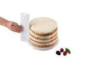 Hand hält einen extra hohen Tortenglätter neben einer mehrschichtigen Torte, seitliche Perspektive.
