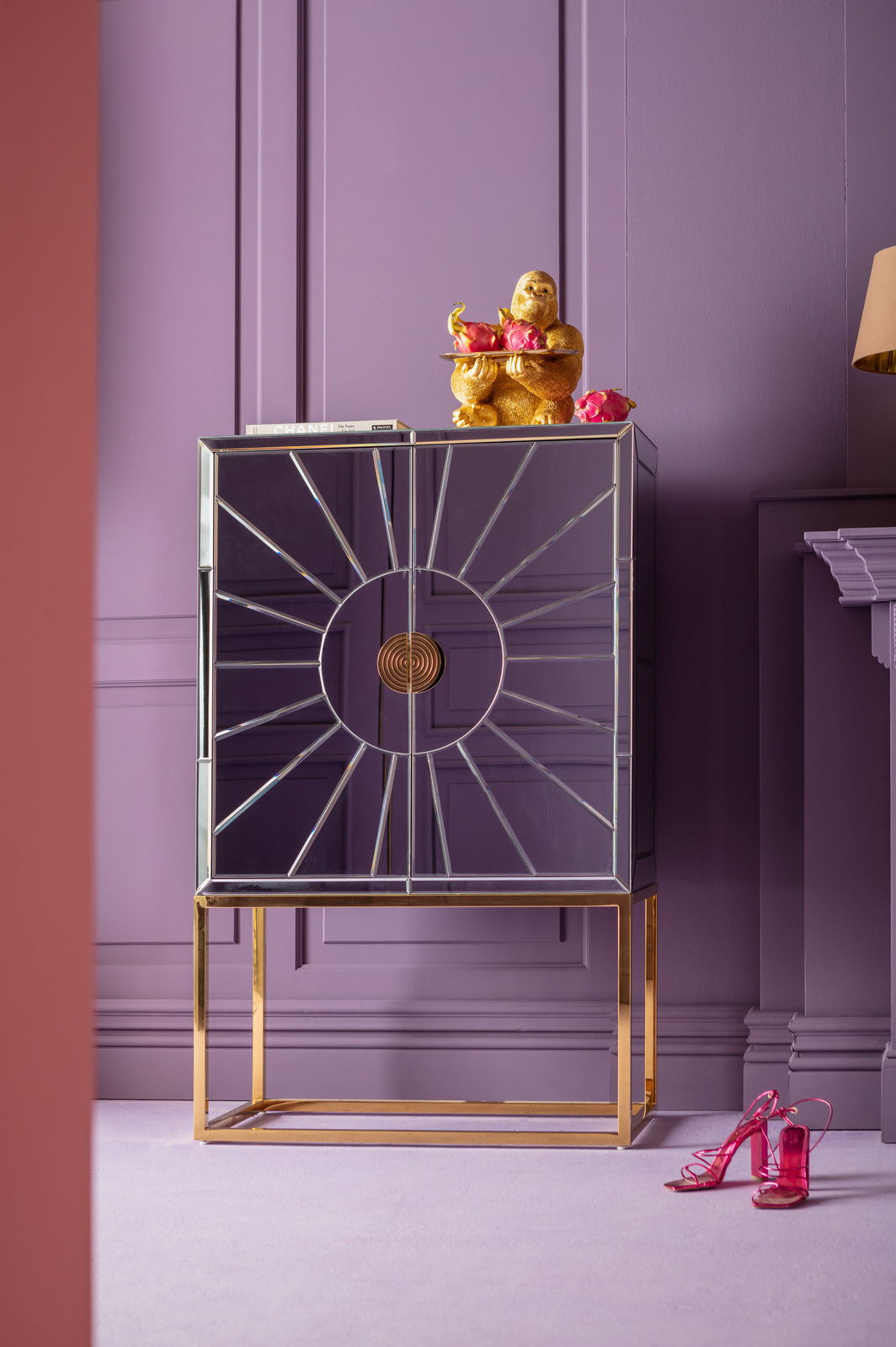 Goldene Gorilla-Dekofigur auf einem modernen, verspiegelten Schrank mit lila Hintergrund, frontal betrachtet.