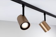 Schwarzes Decken-Stromschienensystem mit zwei zylindrischen LED-Strahlern in Bronze/Gold, ein Spot eingeschaltet; Perspektive: Nahaufnahme in leichter Untersicht von schräg vorn.