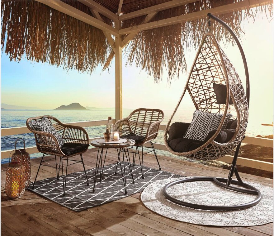 Gartenmöbel-Set auf einer Terrasse mit Meerblick, bestehend aus einem Beistelltisch, zwei Gartensesseln und einem hängenden Loungesessel, aus seitlicher Perspektive fotografiert.