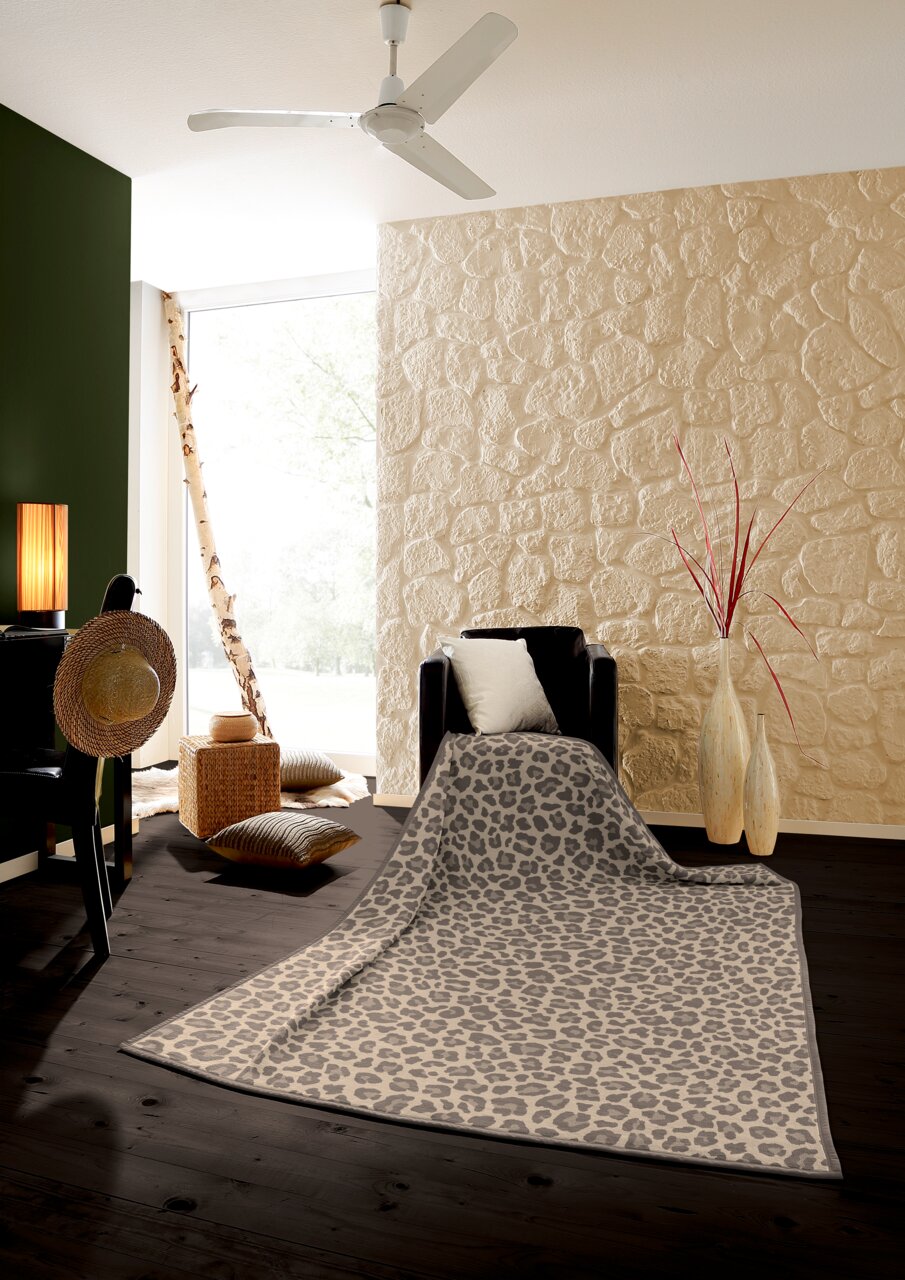 Leopardengemusterte Wohndecke in einem stilvollen Wohnzimmer, drapiert über einem Sessel, mit Blick auf eine moderne Einrichtung mit Steinwand und Holzboden.