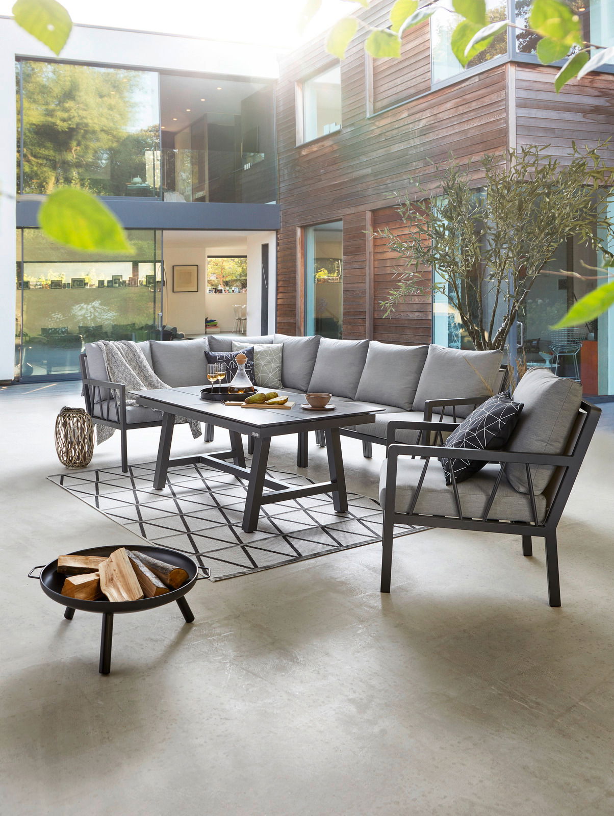 Modernes Lounge-Set in einem stilvollen Innenhof mit grauen Polstern und einem eleganten Tisch, seitliche Perspektive.
