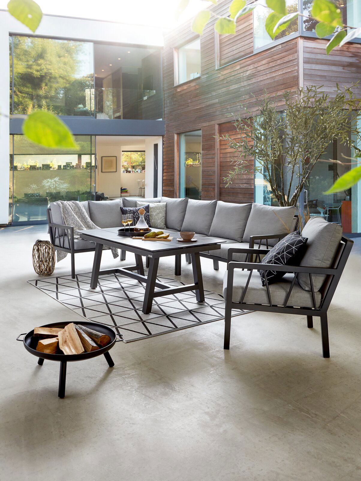 Modernes Lounge-Set in einem stilvollen Innenhof mit grauen Polstern und einem eleganten Tisch, seitliche Perspektive.