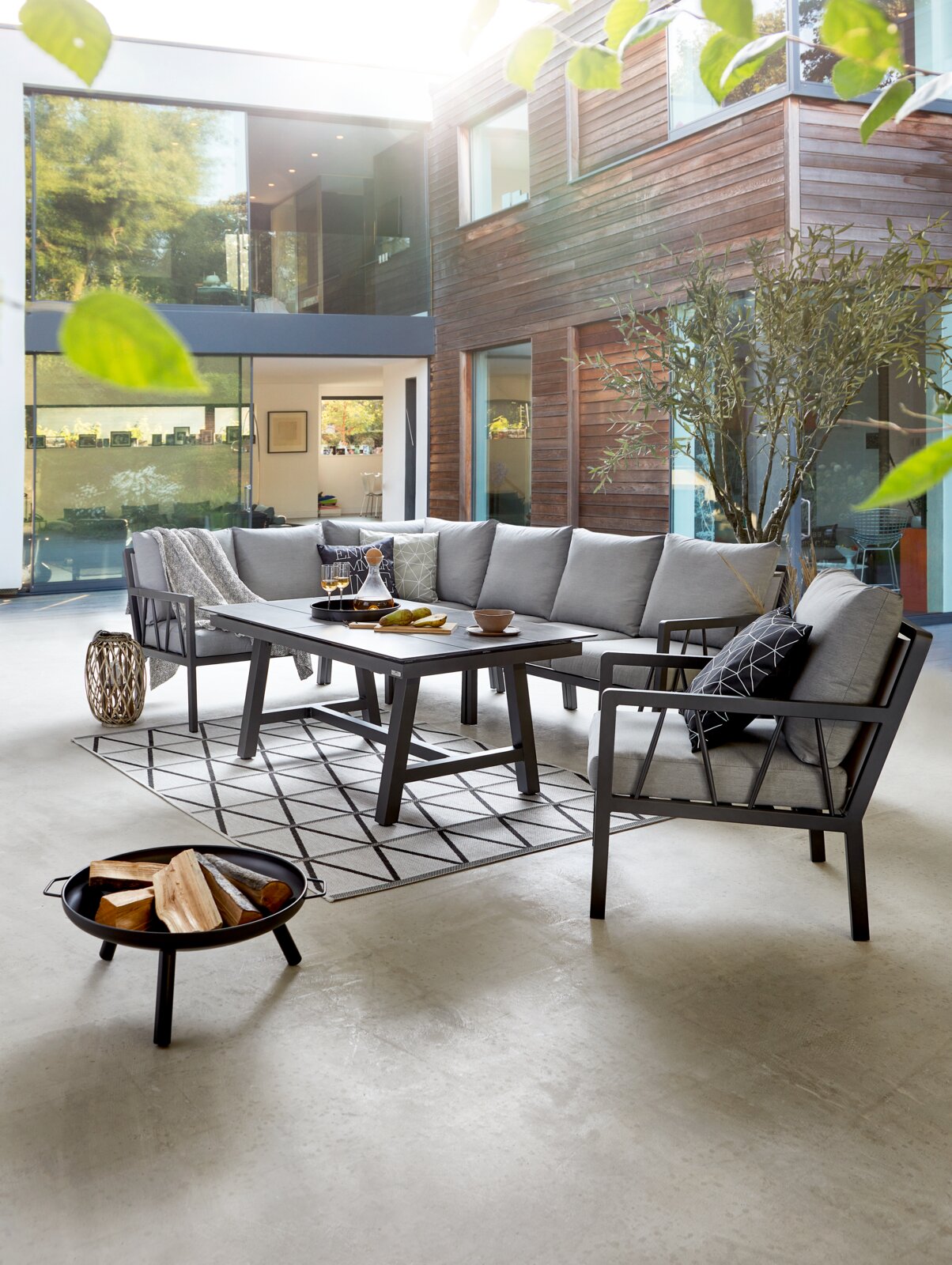 Modernes Lounge-Set in einem stilvollen Innenhof mit grauen Polstern und einem eleganten Tisch, seitliche Perspektive.