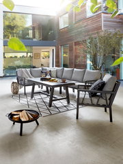 Modernes Lounge-Set in einem stilvollen Innenhof mit grauen Polstern und einem eleganten Tisch, seitliche Perspektive.