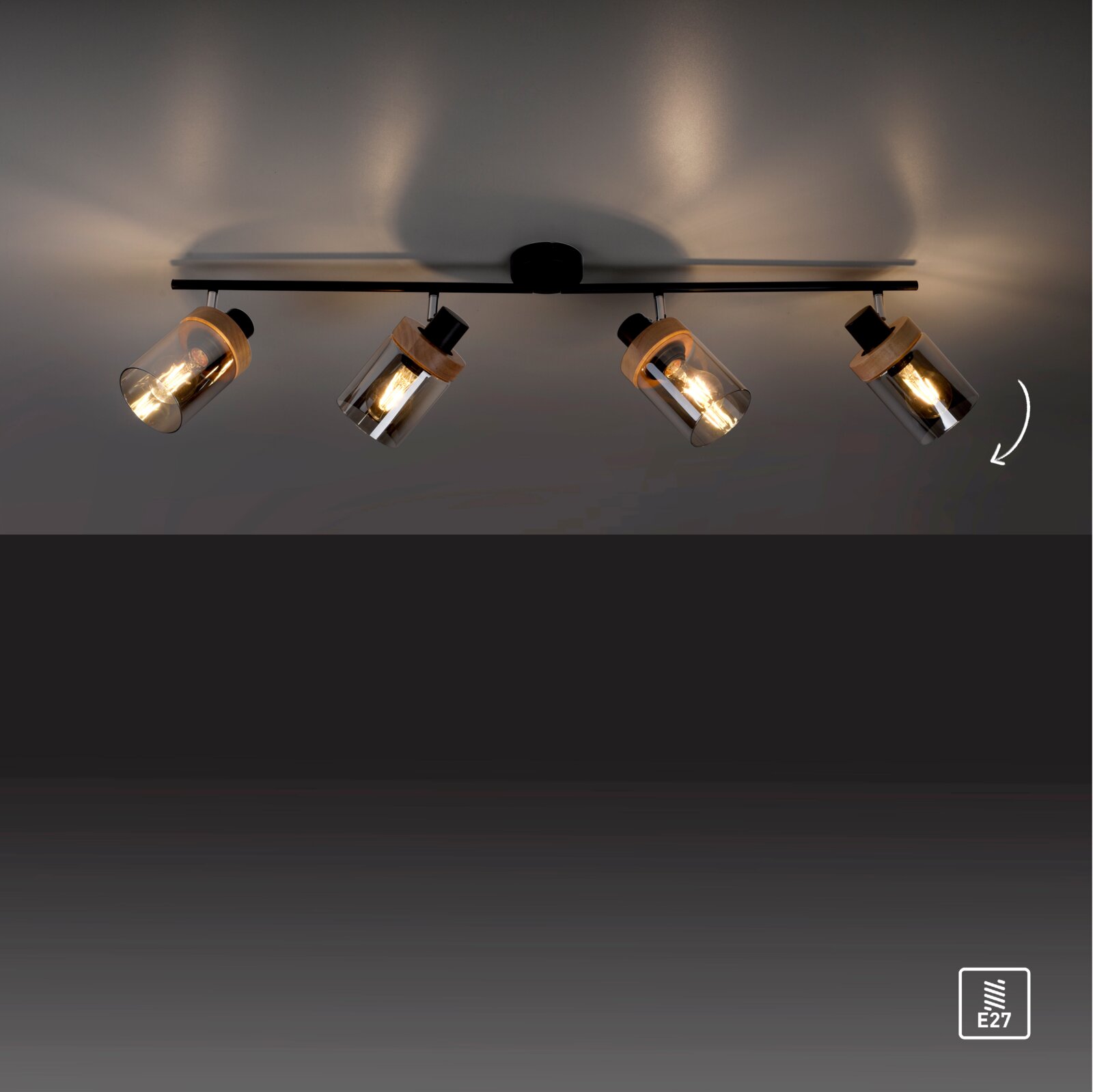 4-flammige Decken-Spotleiste in Schwarz mit schwenkbaren Rauchglas-Zylinderschirmen und Holzdetails, warm leuchtend, Perspektive: Frontalansicht leicht von unten