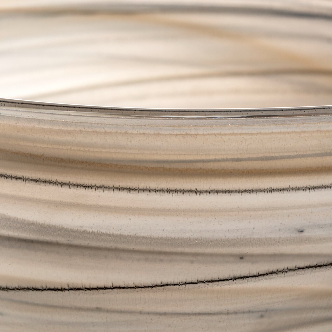 Close-up van een ALABASTRO-schaal in beige en zwart met fijne, horizontale lijnen en een glad oppervlak.
