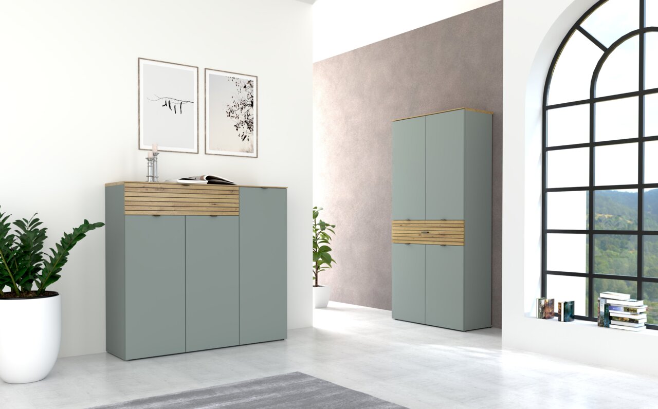 Voleo XL-Schuhschrank DIANA Moderne Garderoben-Sets in einem hellen Raum mit großen Fenstern, bestehend aus einem Sideboard und einem hohen Schrank in Schilfgrün mit Holzakzenten, seitliche Perspektive.