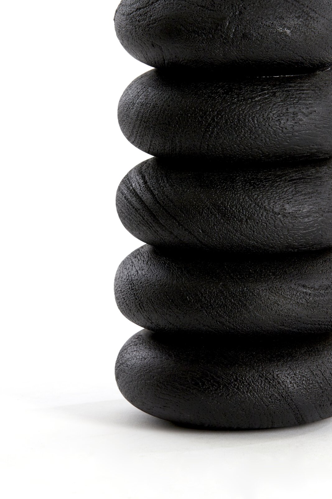 Close-up in zijaanzicht van een zwart sculpturaal object met vijf gestapelde, afgeronde ringen en een subtiel ruwe textuur tegen een witte achtergrond.
