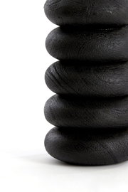Close-up in zijaanzicht van een zwart sculpturaal object met vijf gestapelde, afgeronde ringen en een subtiel ruwe textuur tegen een witte achtergrond.