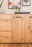 Frontale Ansicht eines Sideboards aus hellem Holz mit Schubladen und Türen, dekoriert mit einer Lampe, einer Weinflasche und Gläsern.