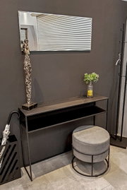 Schmale schwarze Konsole im Flur mit rechteckigem Wandspiegel darüber, dekoriert mit Figurenskulptur und Vase; runder grauer Hocker davor, aufgenommen aus leicht schräger Frontperspektive.