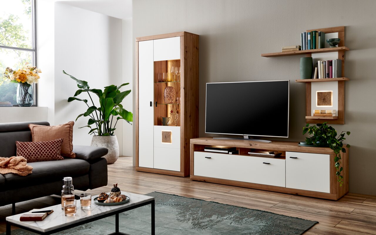 Moderne wandcombinatie BORKUM in een stijlvolle woonkamer, bestaande uit een tv-meubel, een hoge kast met glazen paneel en decoratieve planken. Aanzicht van voren.