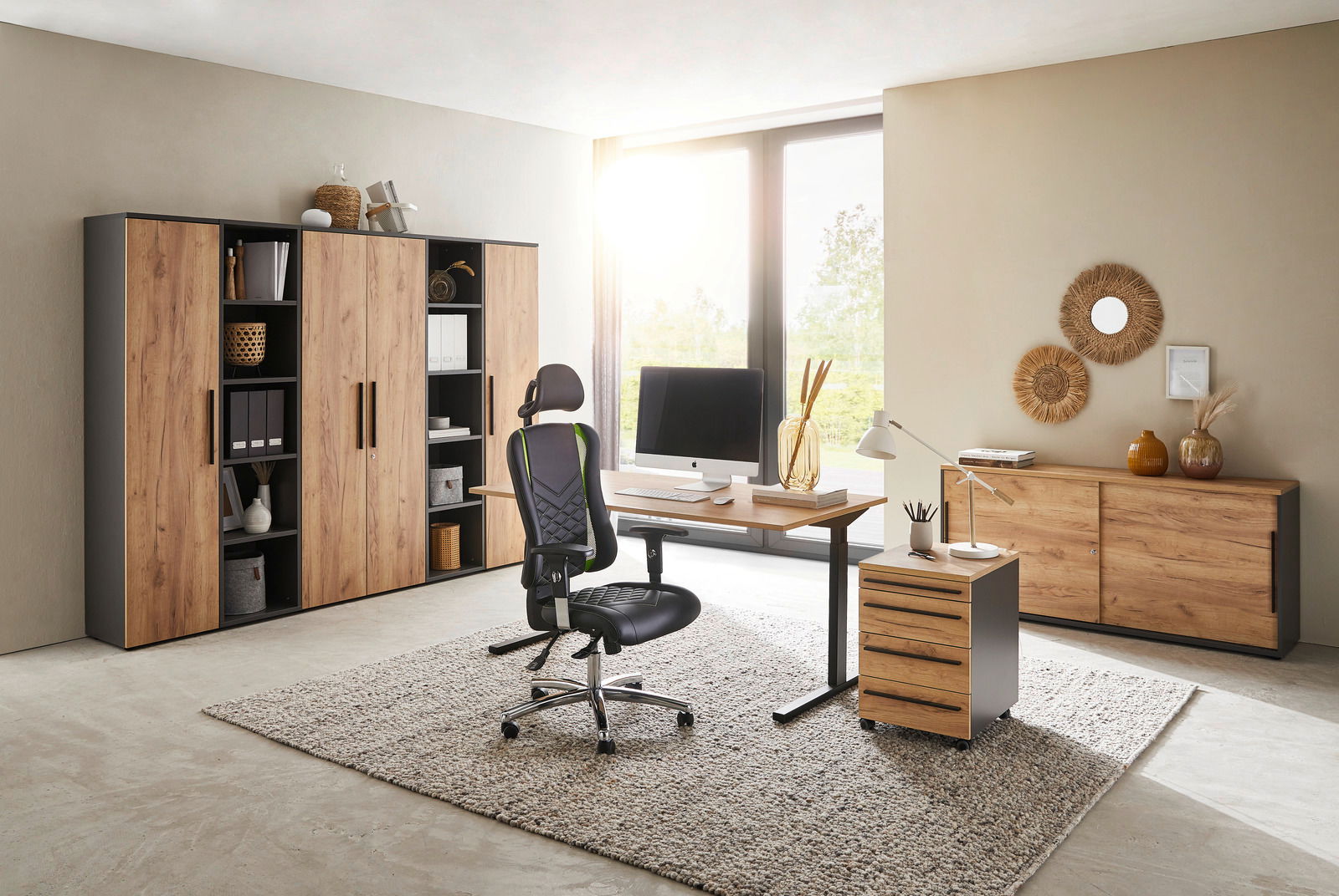 Moderne Büromöbel in einem hellen Raum mit Schreibtisch, Rollcontainer und Aktenschränken in Holzoptik, seitliche Perspektive.