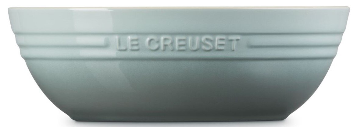 Hellblaue Le Creuset Keramikschüssel mit geprägtem Logo und Rillen, seitliche Frontansicht vor weißem Hintergrund