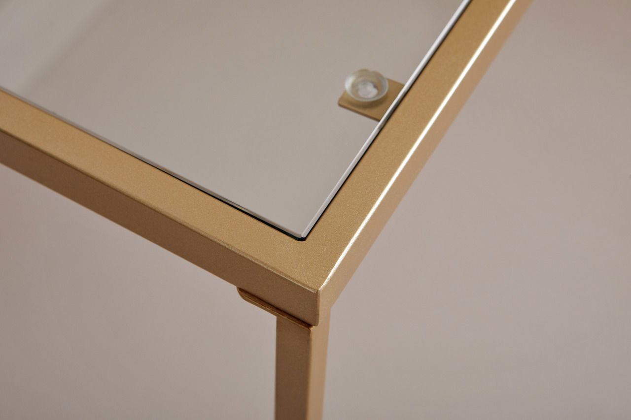 Nahaufnahme einer Ecke eines Schreibtisches mit goldfarbenem Metallrahmen und Glasplatte, von oben betrachtet.