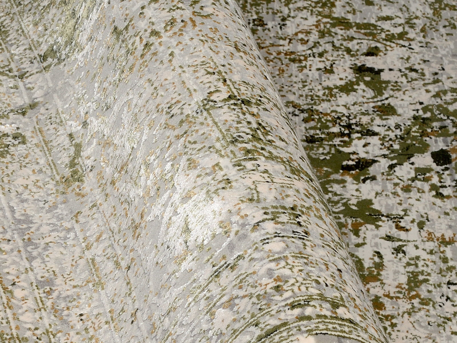 Nahaufnahme eines Designer-Teppichs mit abstraktem Muster in Grün- und Beigetönen, perspektivisch von der Seite aufgenommen.