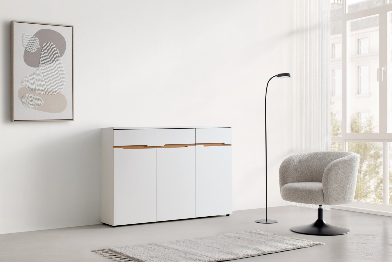 XORA Ladekast MEMPHIS Moderne witte ladekast met houten handgrepen, gefotografeerd van voren, in een minimalistisch ingerichte kamer met een fauteuil, een staande lamp en een abstract wandschilderij.