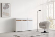 Moderne witte ladekast met houten handgrepen, gefotografeerd van voren, in een minimalistisch ingerichte kamer met een fauteuil, een staande lamp en een abstract wandschilderij.