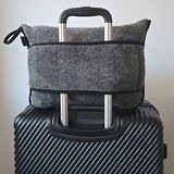 Graue Reisedecke in einer Tasche, die auf einem schwarzen Koffer mit Teleskopgriff befestigt ist, Vorderansicht.