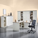 Moderner Eckschreibtisch in heller Holzoptik mit integriertem Stauraum, umgeben von passenden Schränken und einem Bürostuhl, aus der Perspektive eines Betrachters im Raum.