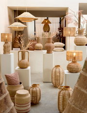 Vase aus geflochtenem Material, umgeben von anderen dekorativen Objekten, aus der Frontalperspektive fotografiert.