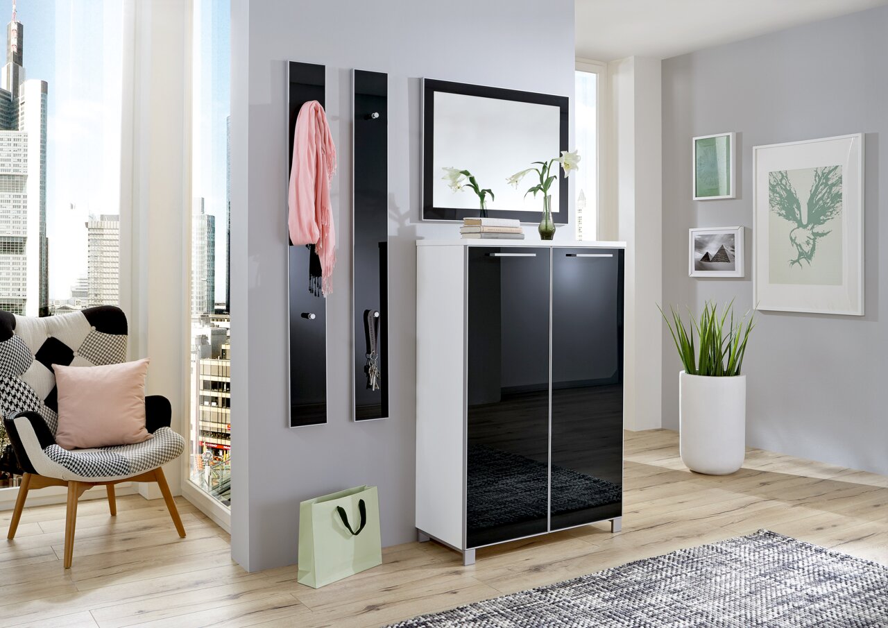 Moderner Eingangsbereich mit einem schwarzen Schuhschrank, zwei schmalen Garderobenpaneelen und einem großen Spiegel. Perspektive von vorne.
