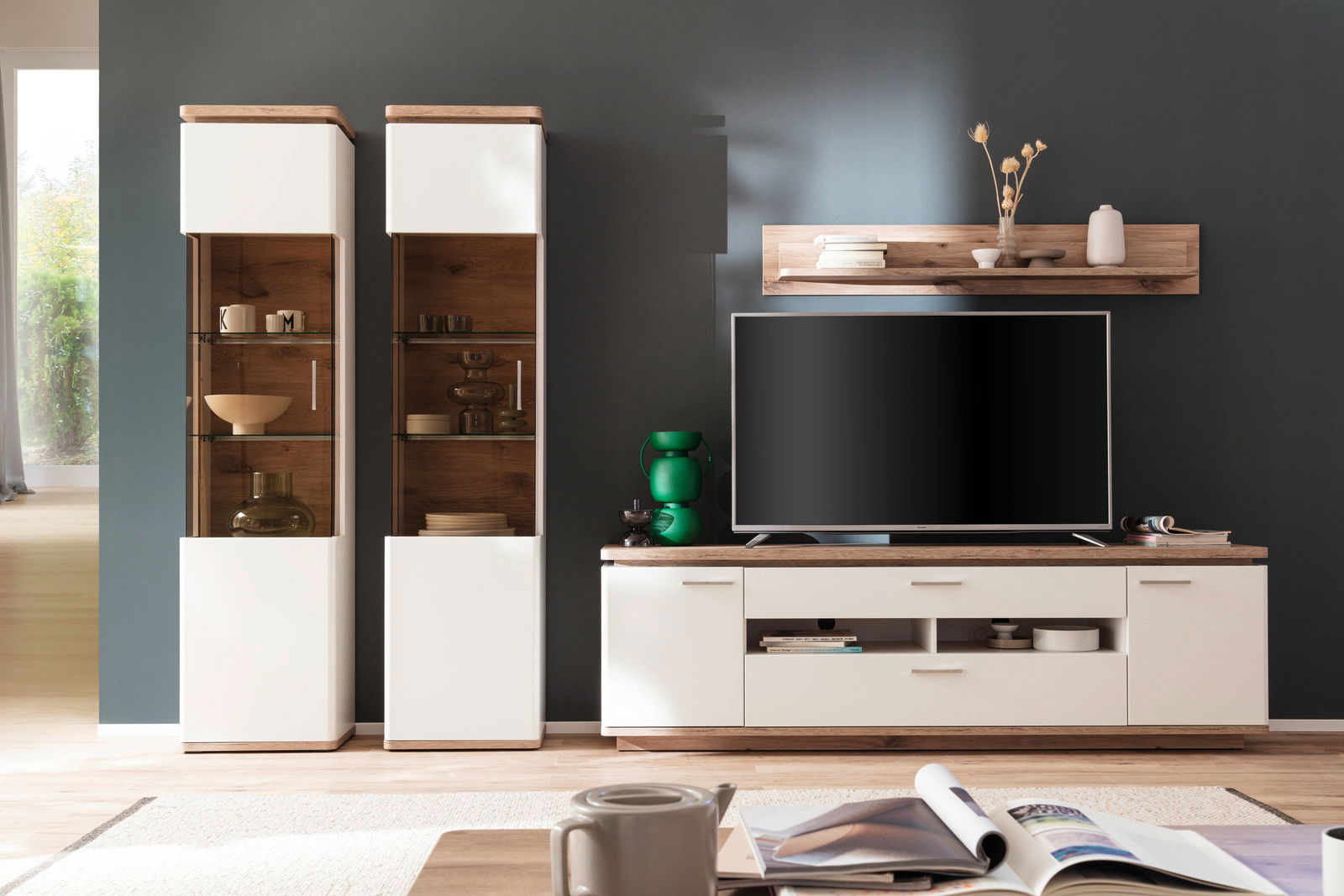 Moderne Wandkombination mit zwei hohen Vitrinen, einem TV-Schrank und einem Wandregal in einem stilvollen Wohnzimmer, frontal betrachtet.