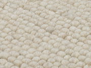 Nahaufnahme eines handgewebten Teppichs mit grober, wolliger Struktur in cremeweißer Farbe.