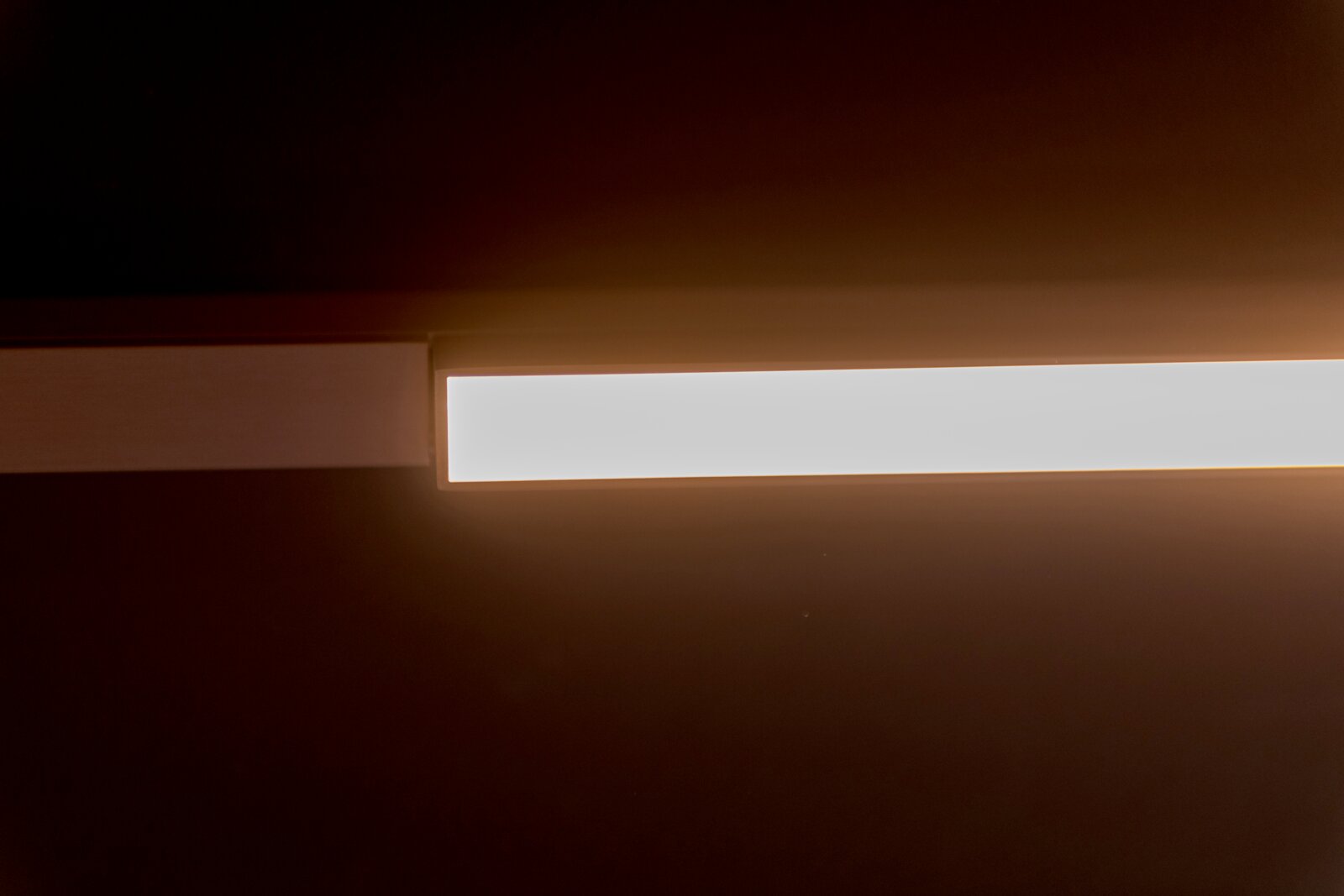 Moderne rechthoekige LED-plafondlamp met warme gloed, gefotografeerd van onderen in perspectief tegen een donkere achtergrond