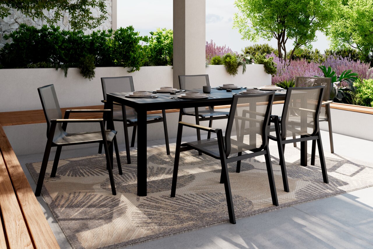 Ambia Garden Stapelstuhl GENET Moderner Stapelstuhl aus schwarzem Metall und Netzgewebe, aufgestellt auf einer Terrasse mit Tisch und Pflanzen im Hintergrund, seitliche Perspektive.