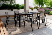 Moderner Stapelstuhl aus schwarzem Metall und Netzgewebe, aufgestellt auf einer Terrasse mit Tisch und Pflanzen im Hintergrund, seitliche Perspektive.