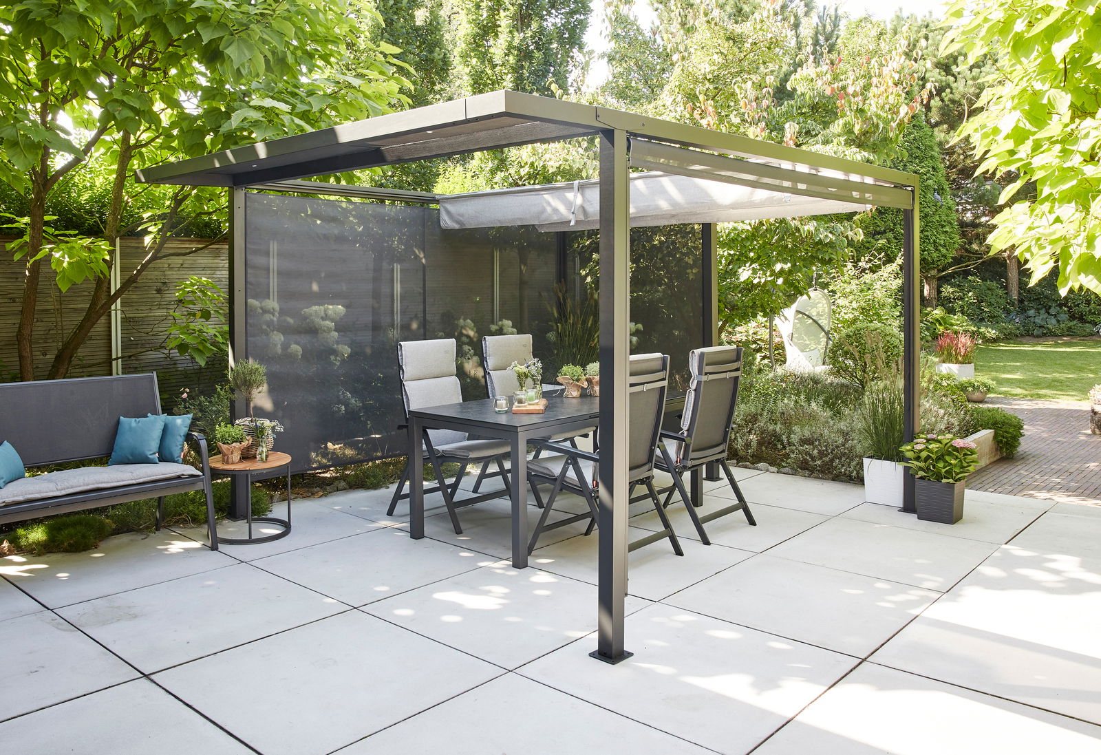 Moderne Pergola mit Faltdach und Sichtschutz, umgeben von Gartenmöbeln und Pflanzen, aus seitlicher Perspektive fotografiert.