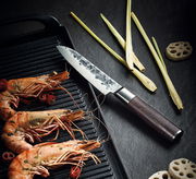 Santokumesser KYOTO 13 cm mit Wengengriff, auf einer dunklen Oberfläche liegend, neben gegrillten Garnelen und Zitronengras, aus der Vogelperspektive.
