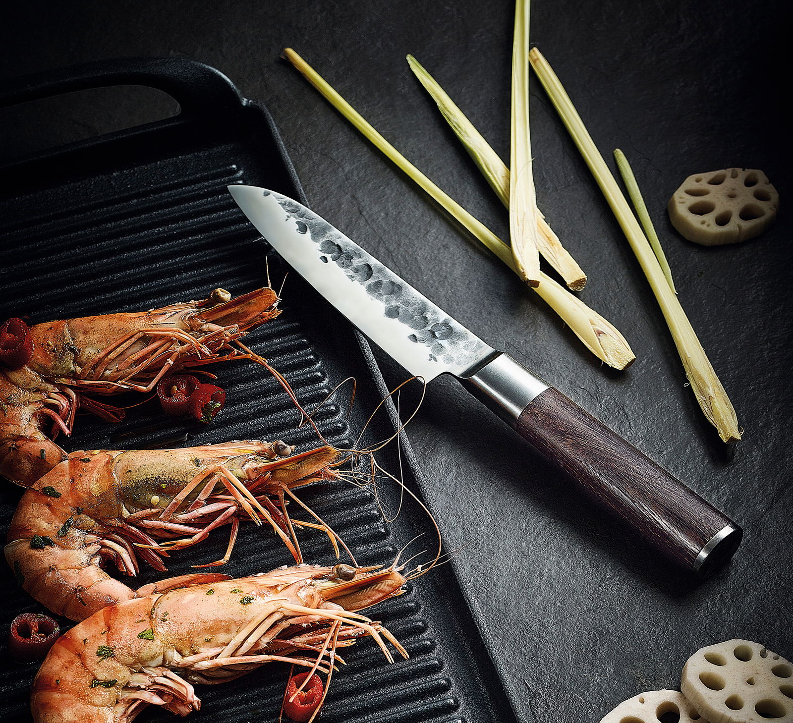 Santokumesser KYOTO 13 cm mit Wengengriff, auf einer dunklen Oberfläche liegend, neben gegrillten Garnelen und Zitronengras, aus der Vogelperspektive.