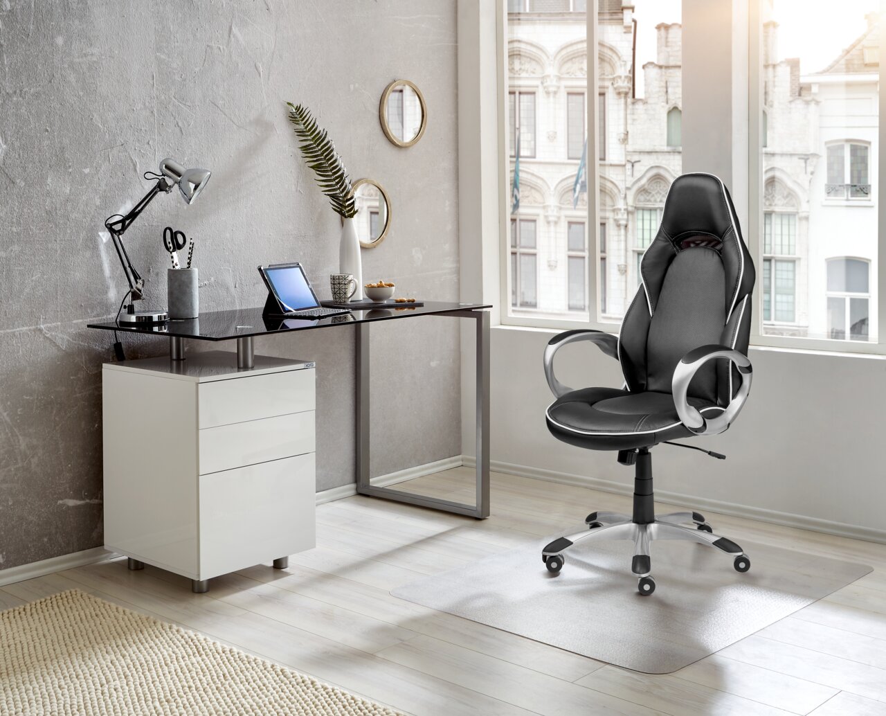 Moderner Schreibtisch mit Glasplatte und weißem Unterschrank, seitliche Perspektive, in einem stilvollen Büro mit ergonomischem Bürostuhl.