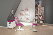 Moderne draaistoel voor jongeren in een stijlvolle kinderkamer, met een roze zitting en rugleuning, voor een bureau met planken op de achtergrond. Aanzicht van voren.