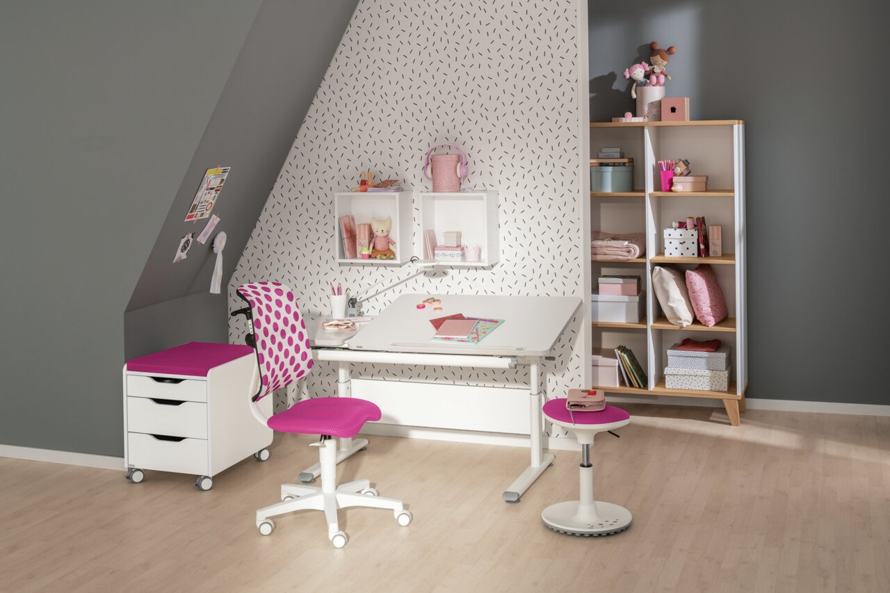 Moderne draaistoel voor jongeren in een stijlvolle kinderkamer, met een roze zitting en rugleuning, voor een bureau met planken op de achtergrond. Aanzicht van voren.