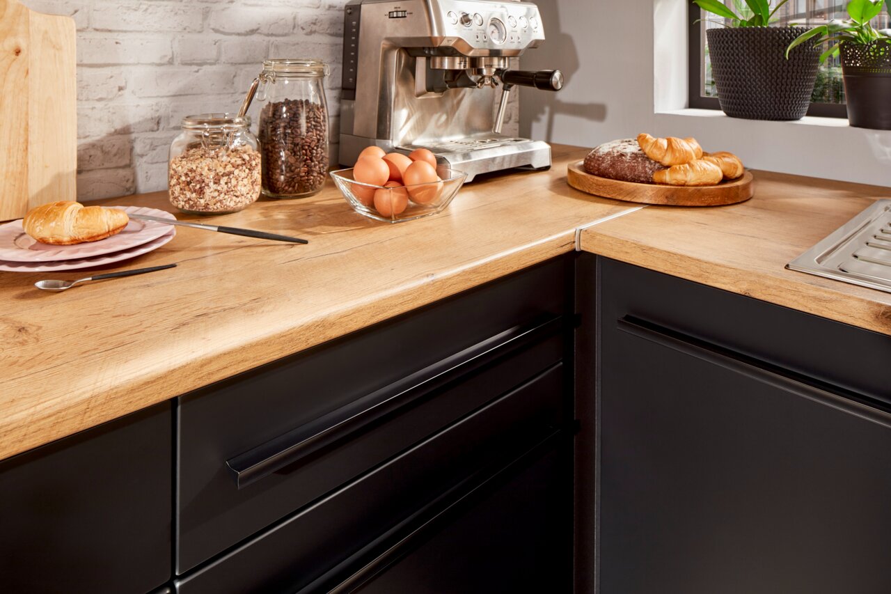 Moderne Küche mit Eckunterschrank, Holzarbeitsplatte und schwarzen Schubladen, aus der Vogelperspektive fotografiert.