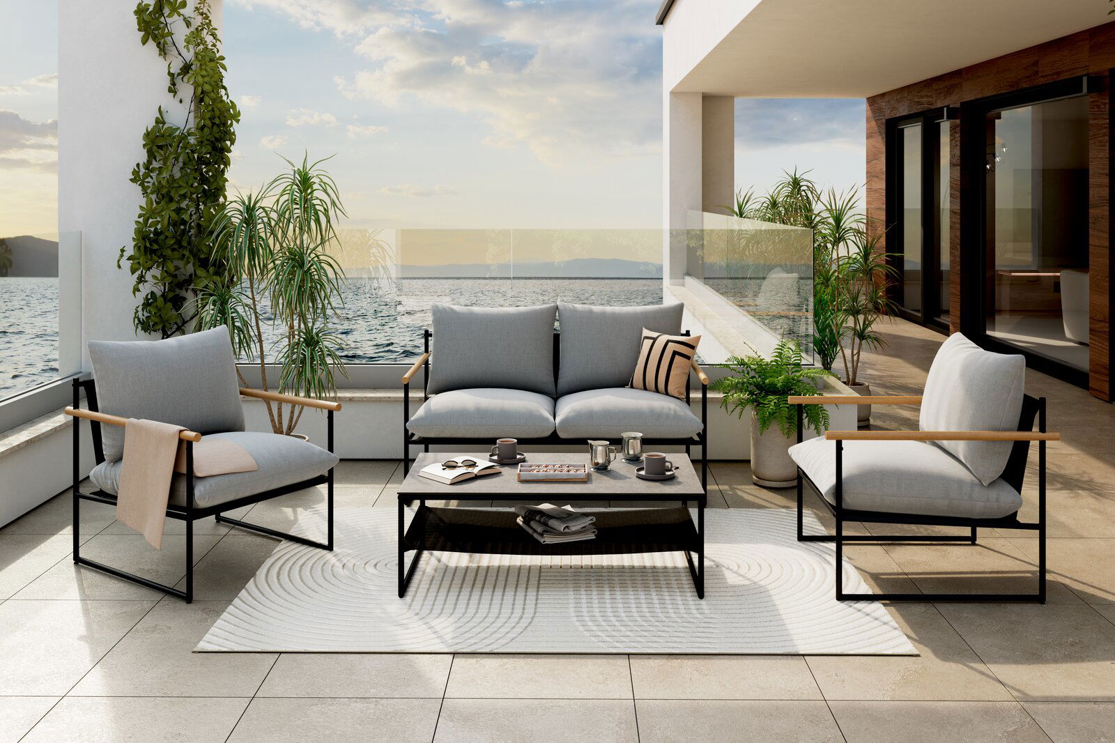 Gartenlounge-Set auf einer Terrasse mit Meerblick, bestehend aus einem Sofa, zwei Sesseln und einem Tisch, umgeben von Pflanzen. Perspektive von vorne.