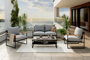 Gartenlounge-Set auf einer Terrasse mit Meerblick, bestehend aus einem Sofa, zwei Sesseln und einem Tisch, umgeben von Pflanzen. Perspektive von vorne.