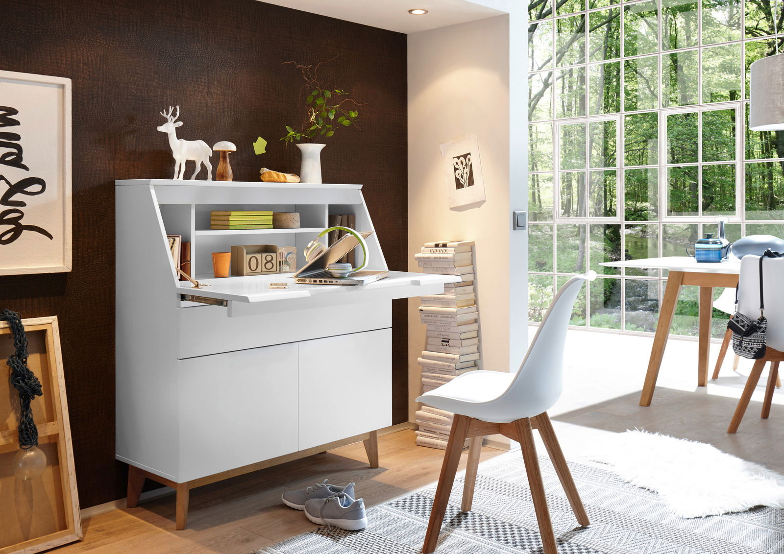 Novel Sekretär BLANC Moderner weißer Sekretär mit ausklappbarer Arbeitsfläche, umgeben von stilvoller Dekoration und natürlichem Licht, seitliche Perspektive.