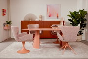 Esszimmer mit einem ovalen Tisch und mehreren Armlehnstühlen in Rosa, moderne Einrichtung mit Pflanzen und Kunstwerken, seitliche Perspektive