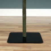 Nahaufnahme des unteren Teils eines künstlichen Weihnachtsbaums mit einem stabilen schwarzen Metallständer auf einem Holzboden.