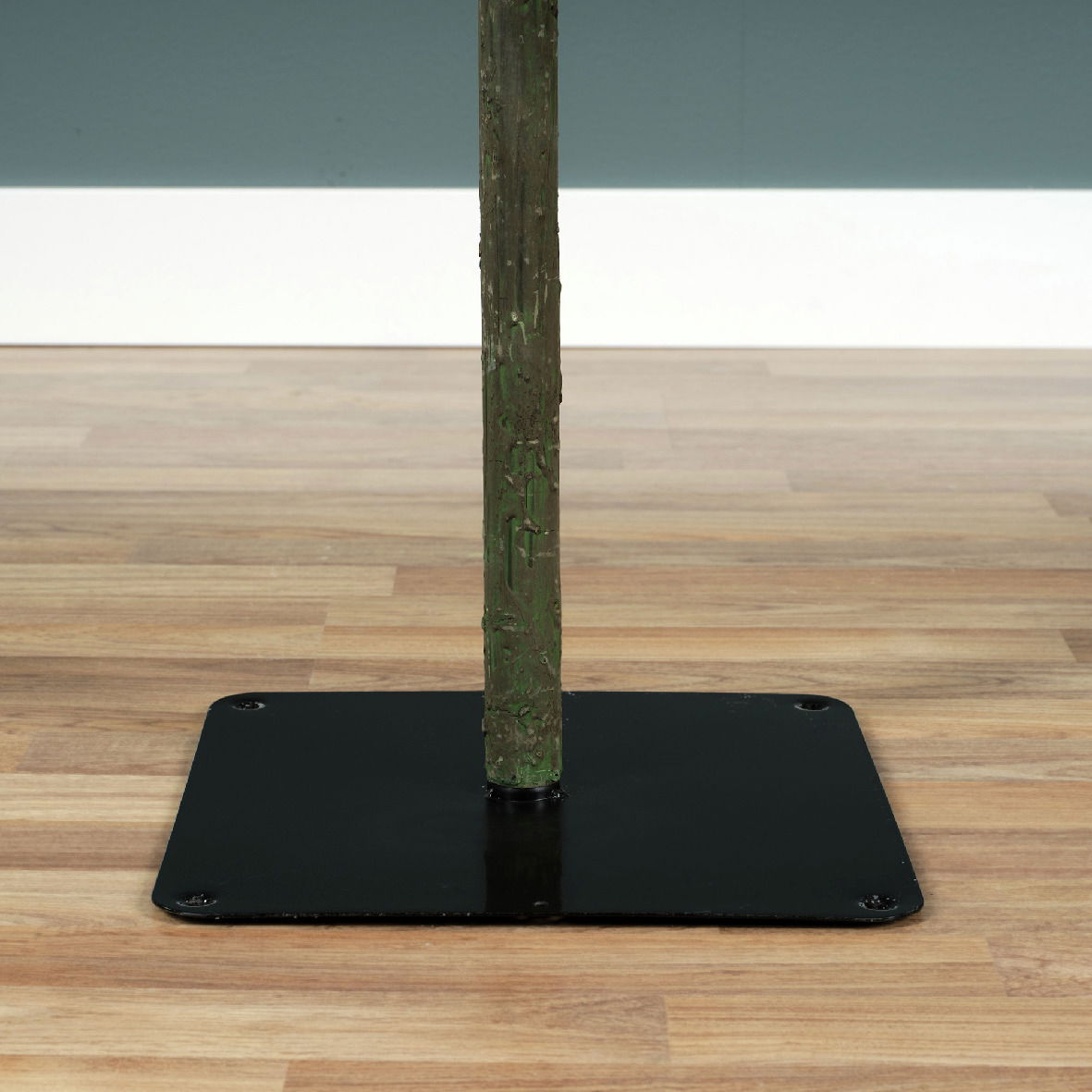 Nahaufnahme des unteren Teils eines künstlichen Weihnachtsbaums mit einem stabilen schwarzen Metallständer auf einem Holzboden.